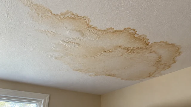 Large brown water stain spreading across an interior ceiling